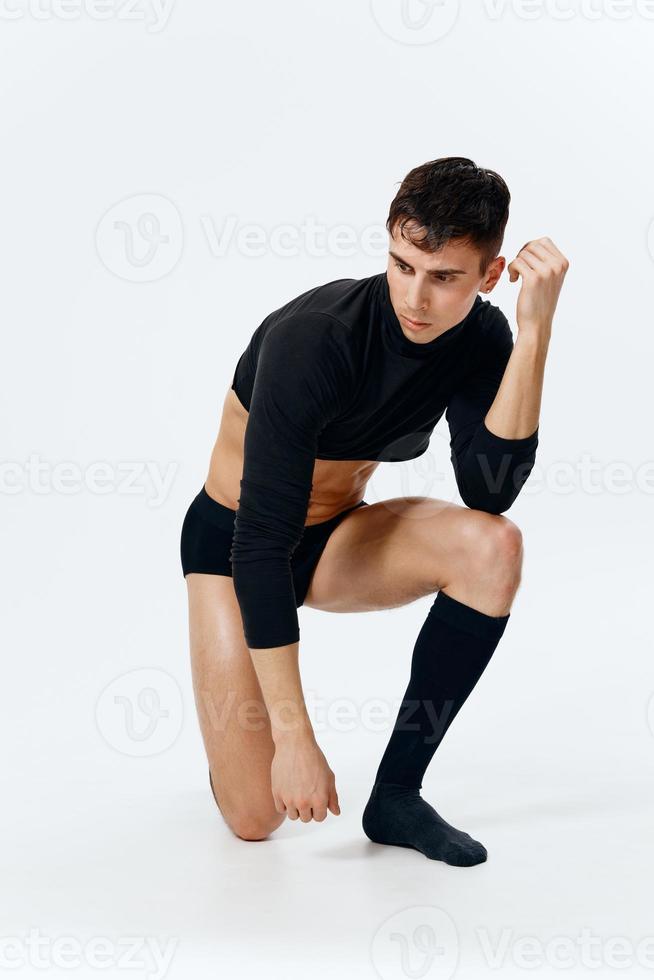 a sporty man in black shorts and a short sweater on a light background stands on his knee in full growth photo