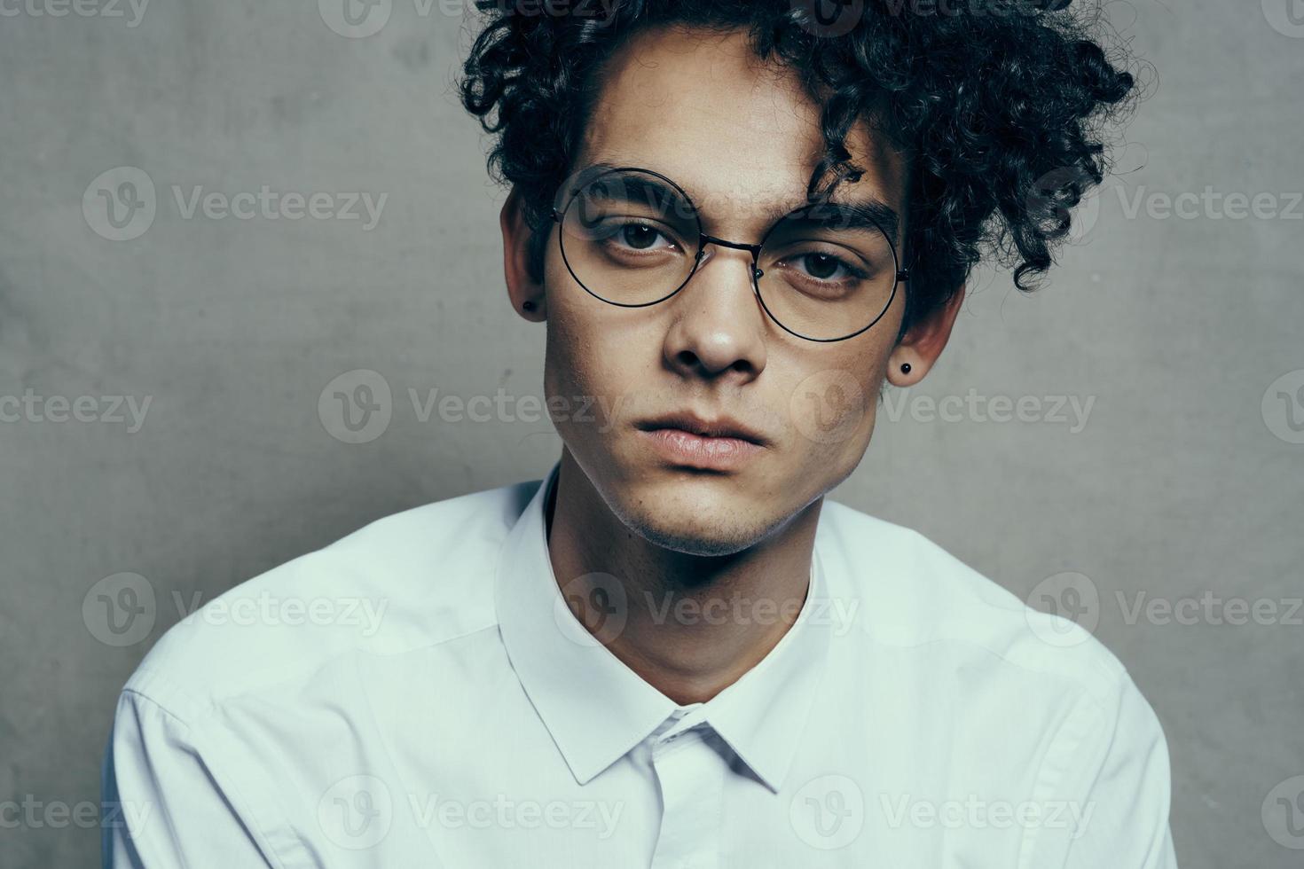 portrait of a nice guy with curly hair on a gray background and a light shirt glasses model close-up photo