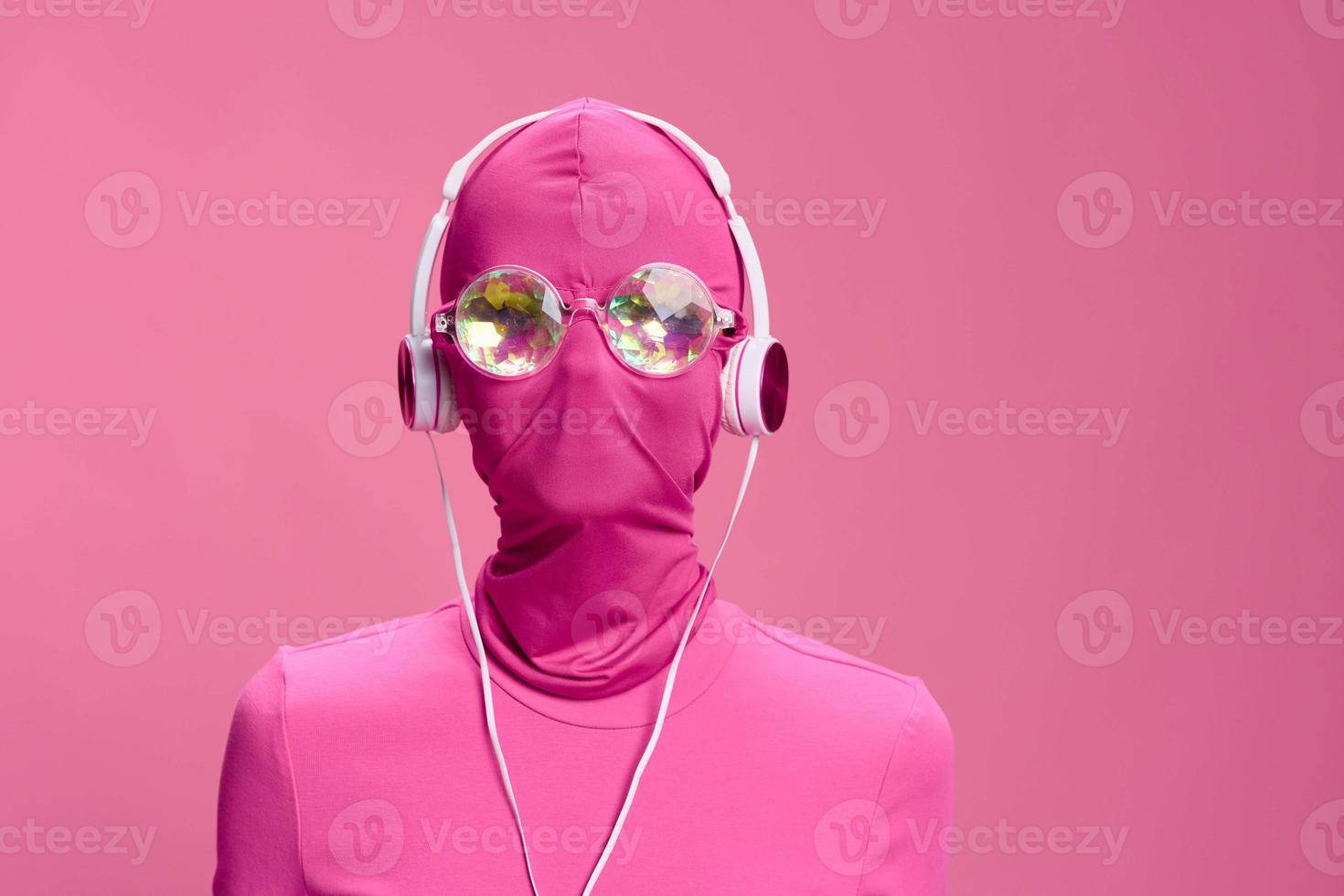 Creative fan art photo of a young female cyberpunk blogger on a pink background wearing a pink full-face mask with glowing round glasses and headphones