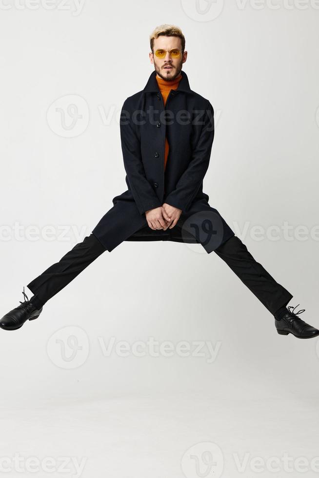 energetic man jumped up with legs wide apart in a black coat photo