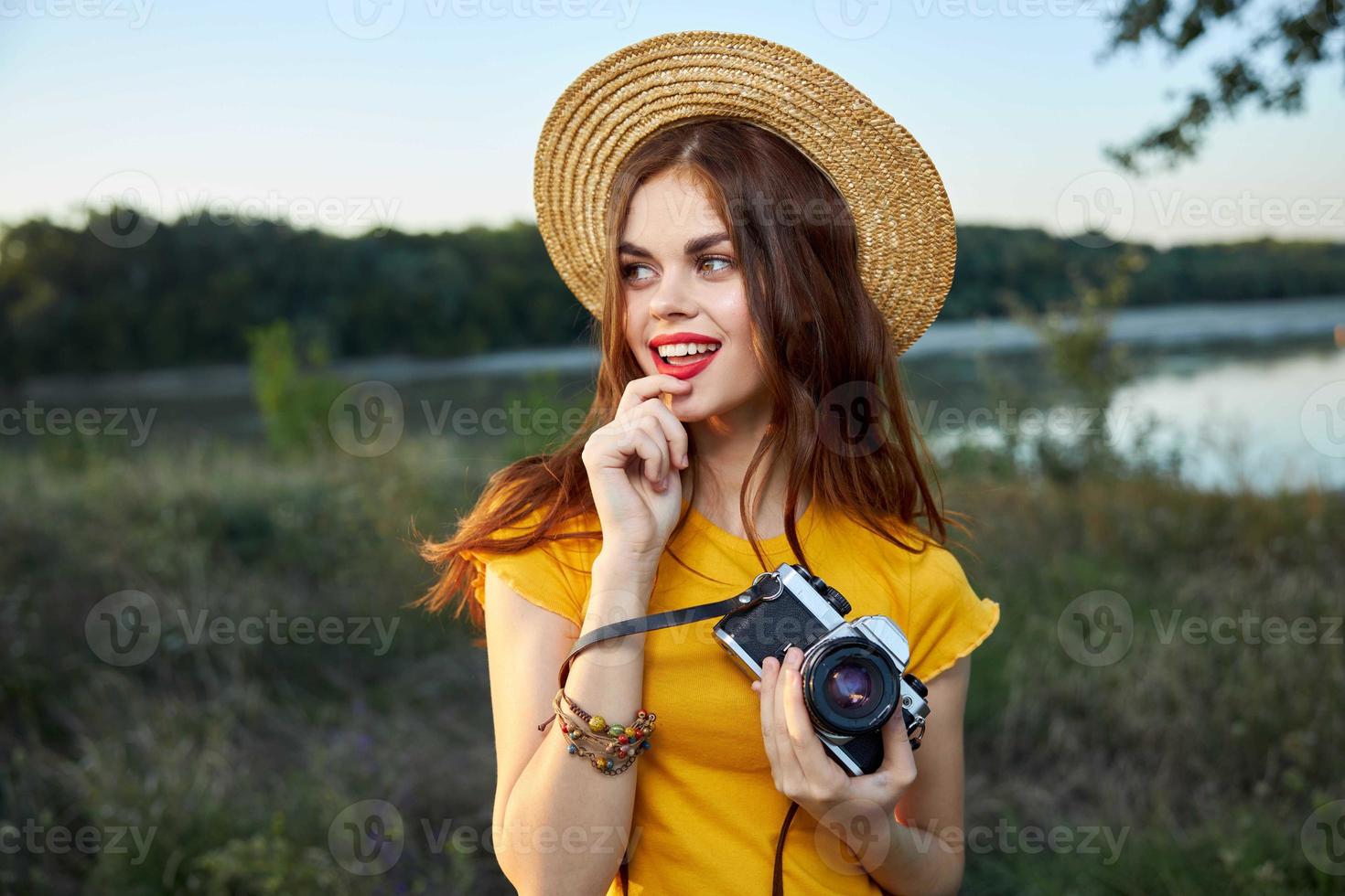 Woman with a camera in her hands wearing a hat red lips look aside nature photo