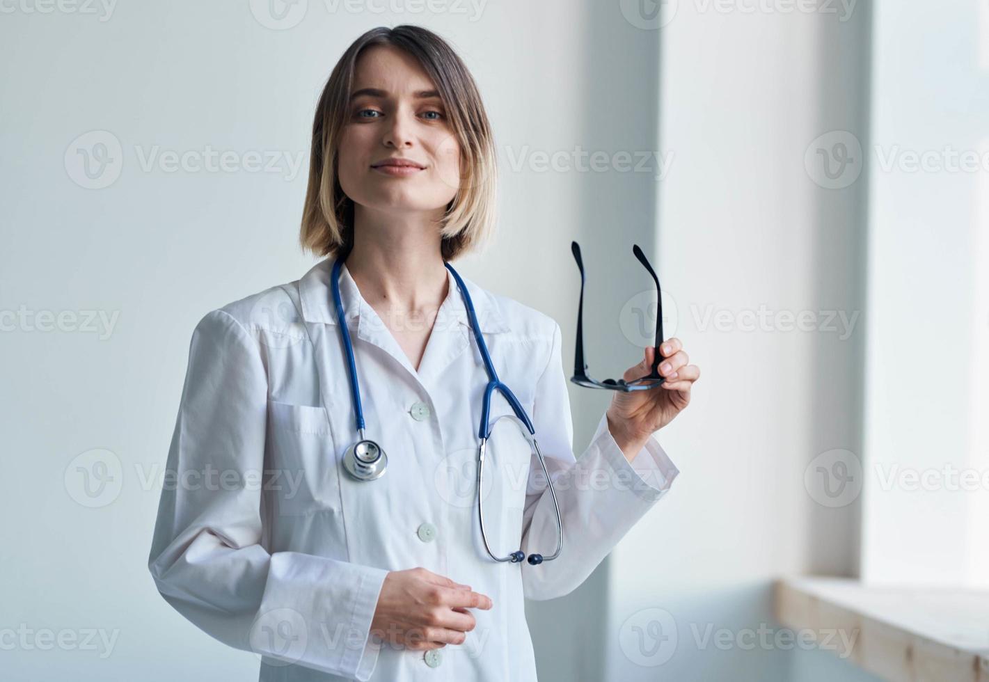 profesional médico mujer participación lentes en su mano y estetoscopio alrededor su cuello foto