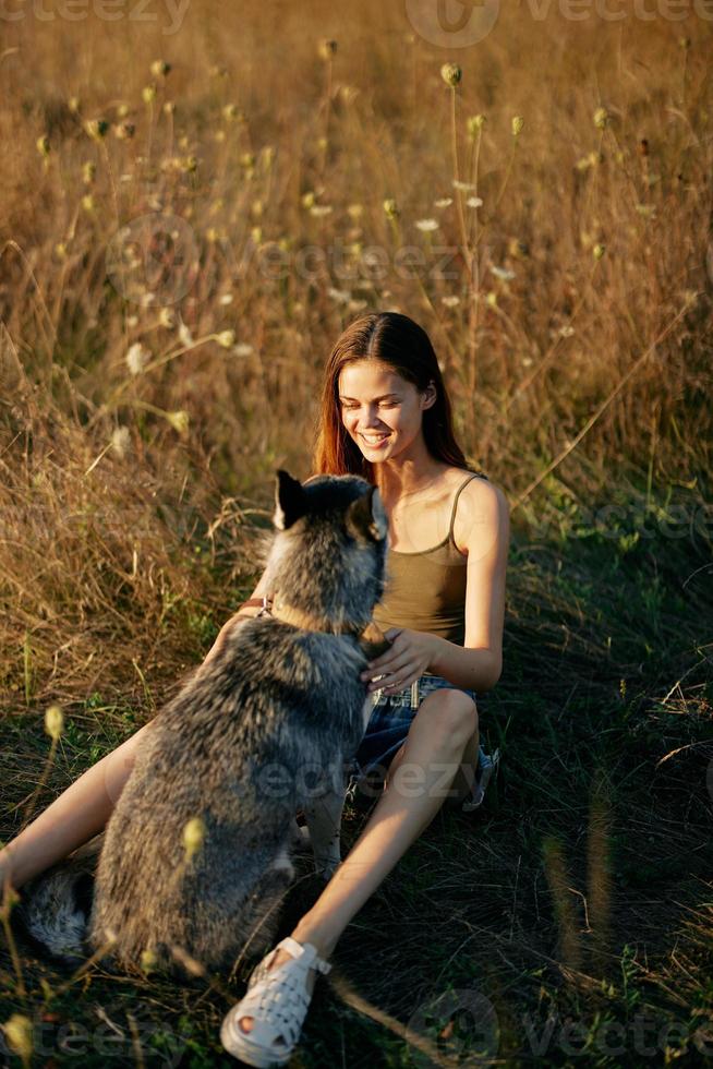 Woman sitting in a field with a dachshund dog smiling while spending time in nature with a friend dog in autumn at sunset photo
