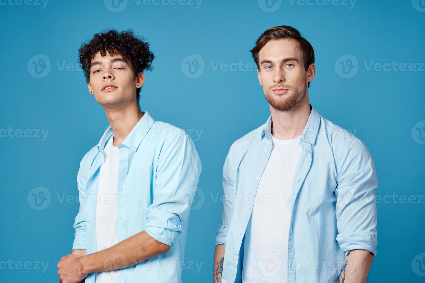 two friends in identical shirts and a t-shirt gesturing with their hands on a blue background photo