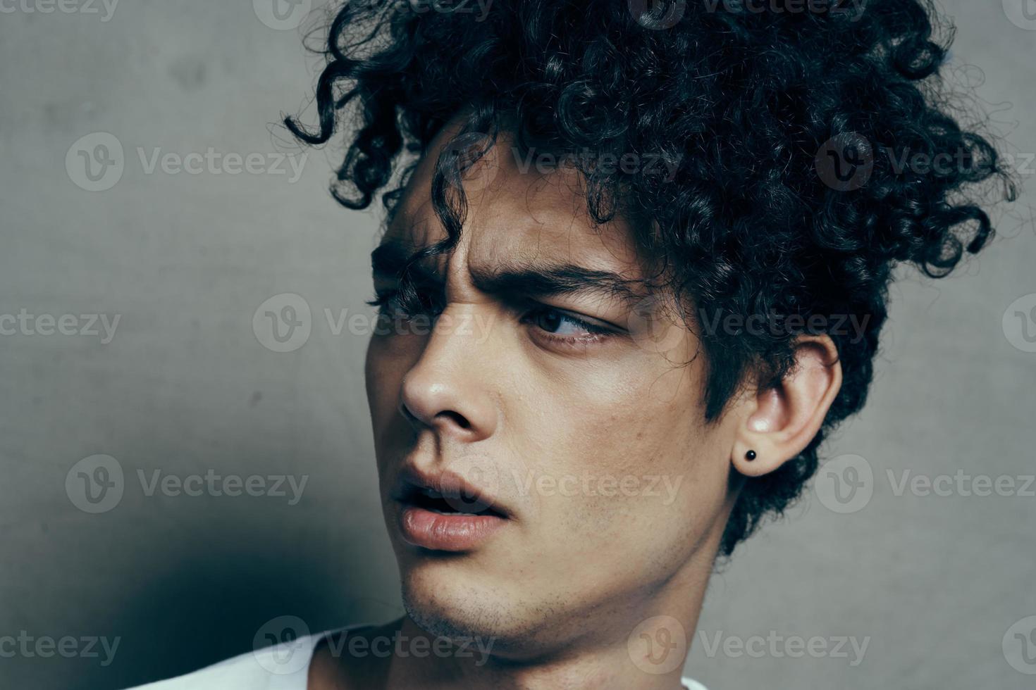 portrait of a handsome guy with curly hair on a gray background white t-shirt close-up model photo