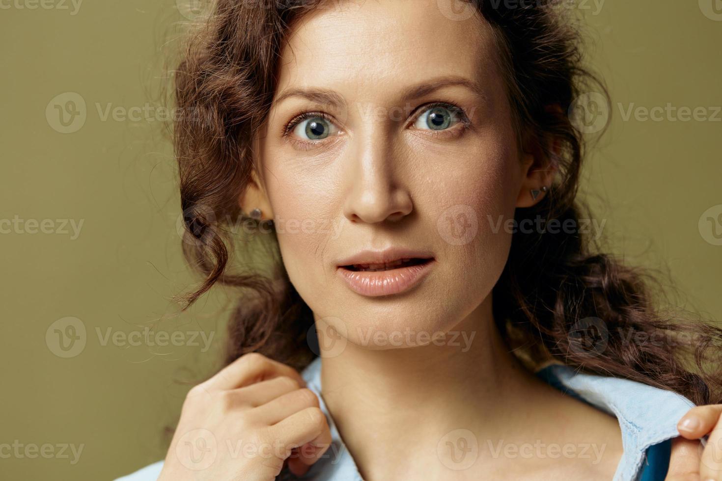 Serious adorable curly beautiful female in jeans casual shirt touches collar looks at camera posing isolated on olive green background. Being Yourself. People Lifestyle emotions concept. Copy space photo