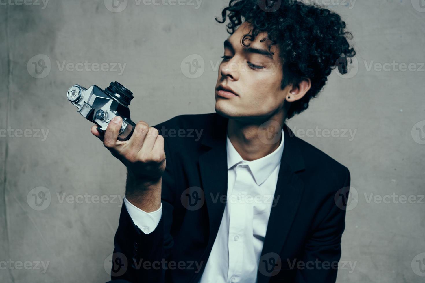 curly-haired man in a classic suit looks at the camera in his hand studio hobby photo