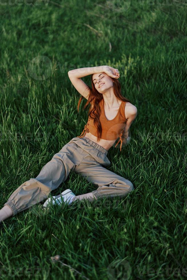 A woman lies on fresh spring green grass in a park without mosquitoes or ticks and enjoys relaxing while watching the sunset. The concept of safe outdoor recreation photo