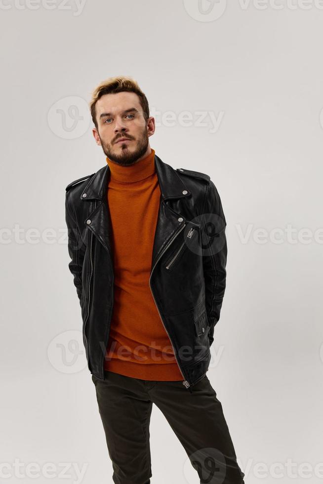 fashionable car with a leather jacket and an orange sweater holds his hands behind a belt and brown trousers photo