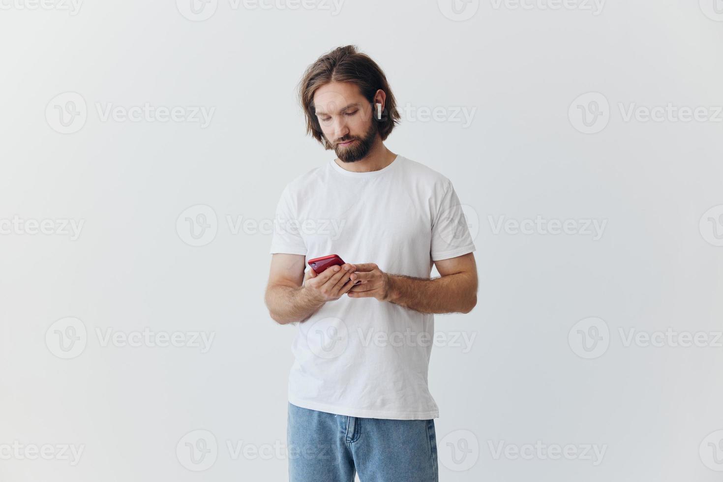 A man is holding a phone with wireless headphones in his ears and reading a social media message online freelancer job correspondence on a white background photo