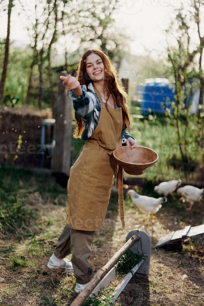 A young woman works on a farm and pours fresh feed from a bowl to feed the chickens and makes sure the food is clean and organic for the health of the faces and chickens photo