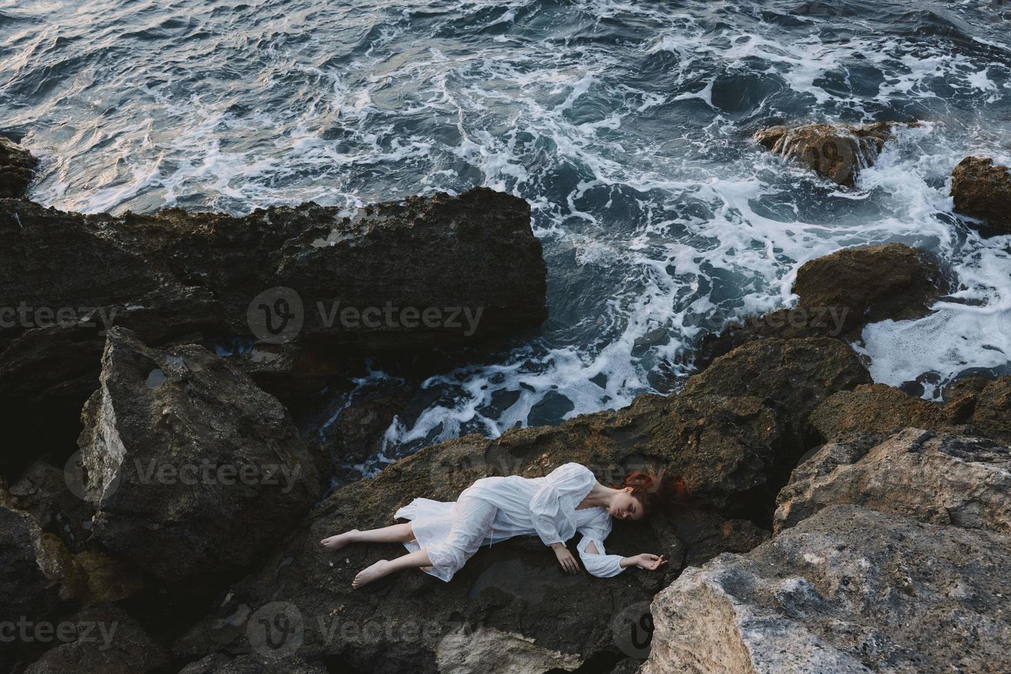 hermosa mujer en un aislado Mancha en un salvaje rocoso costa en un blanco vestir vacaciones concepto foto