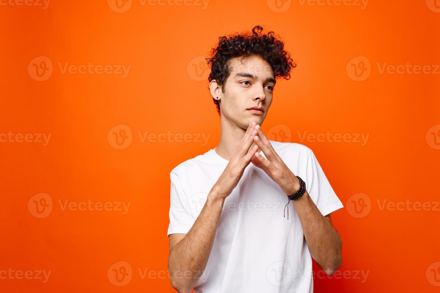 curly guy in a white t-shirt gesturing with his hand on an orange background photo