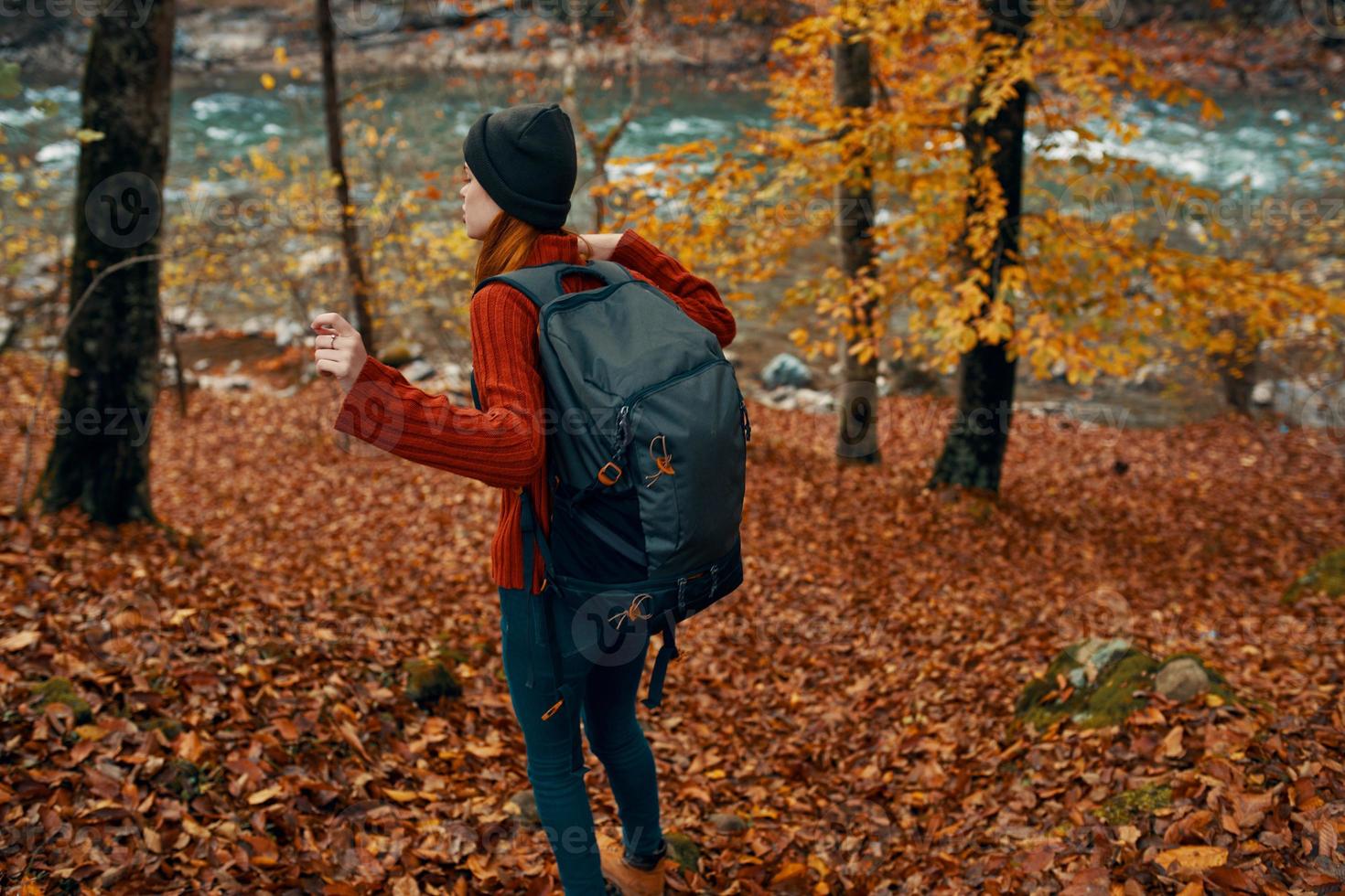 mujer en un suéter con un mochila y en pantalones camina mediante el otoño bosque en el montañas cerca el río foto