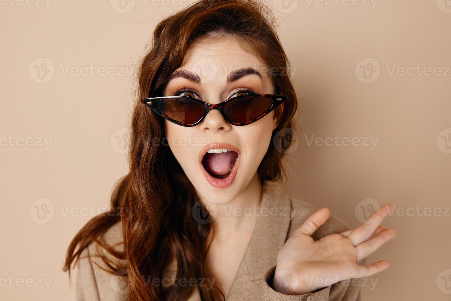 woman in glasses with open mouth and gesturing with hands beige background photo