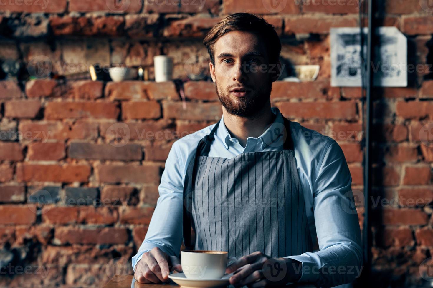 masculino camarero delantal Servicio café taza ladrillo pared foto