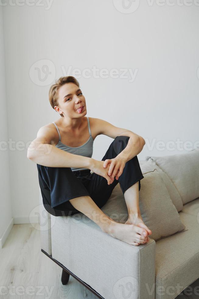 Teenage girl sitting on the couch at home smiling in home clothes and glasses with a short haircut, lifestyle without filters, free copy space photo