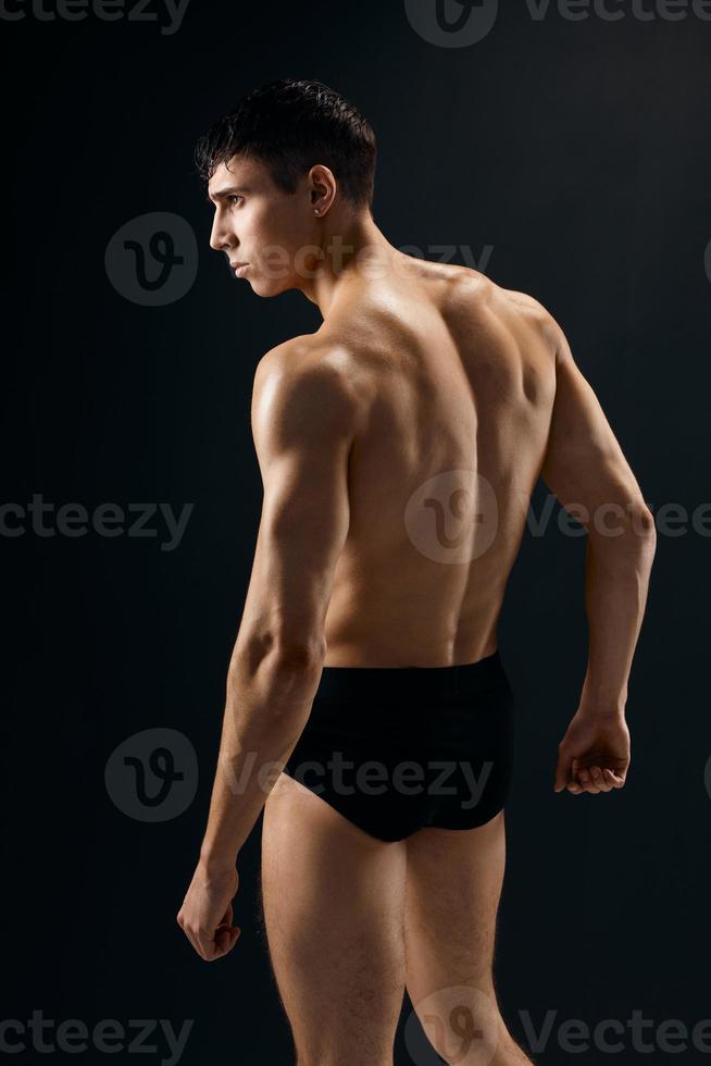 a handsome man bodybuilder with a pumped-up body stands with his back dark background photo