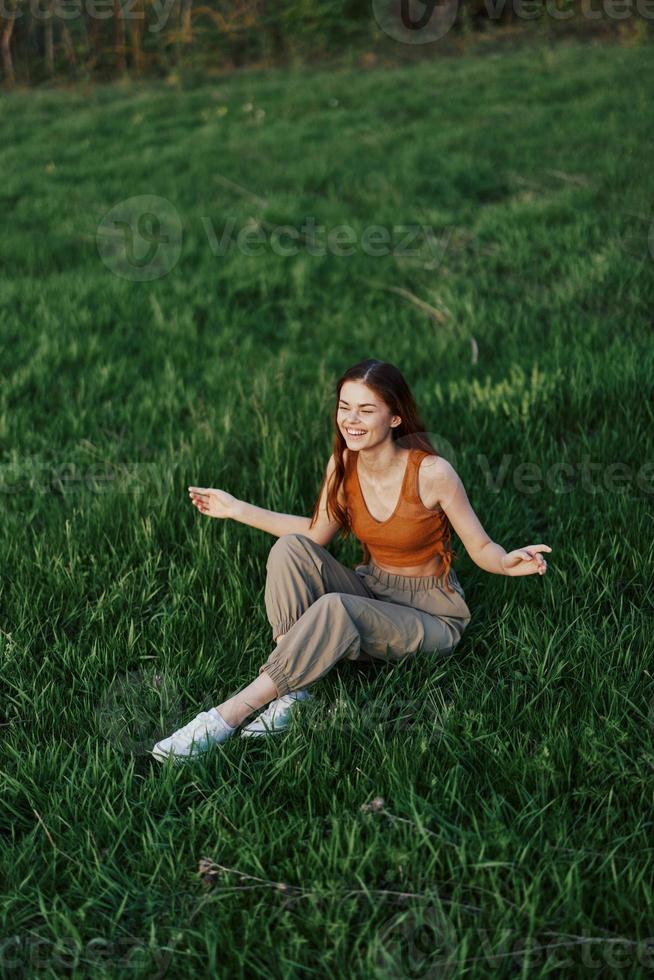 A woman enjoying the outdoors sitting in the park on the green grass in casual clothing with long flowing hair, lit by the bright summer sun without mosquitoes photo