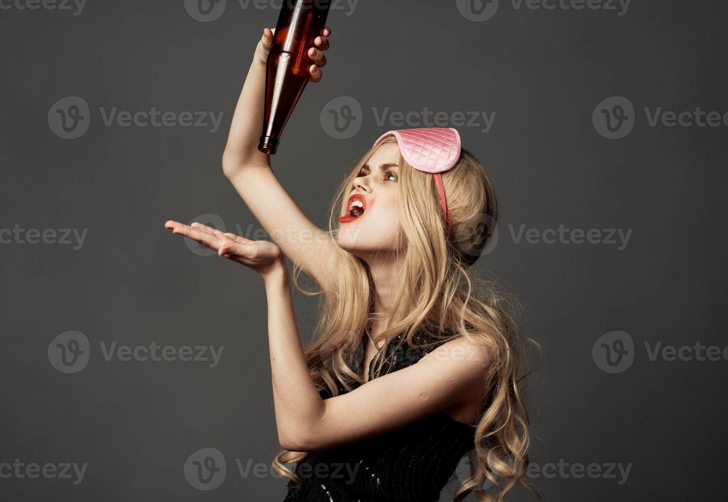 Woman holding a bottle with alcohol in her hands on a gray background black dress sleep mask photo