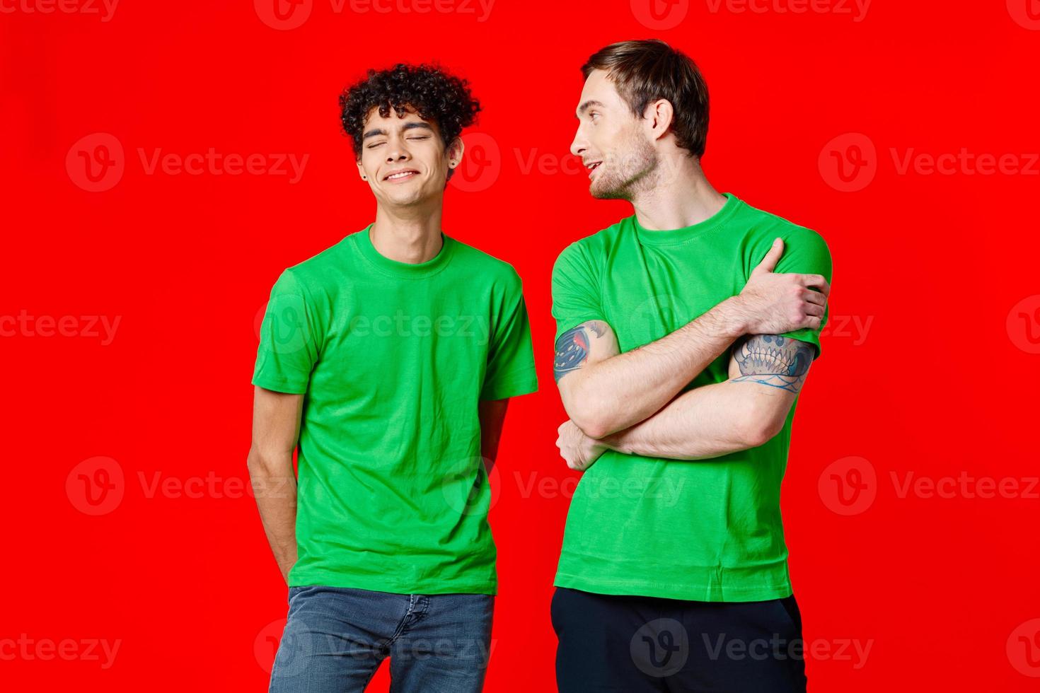 joyful friends in green t-shirts are standing next to red background photo