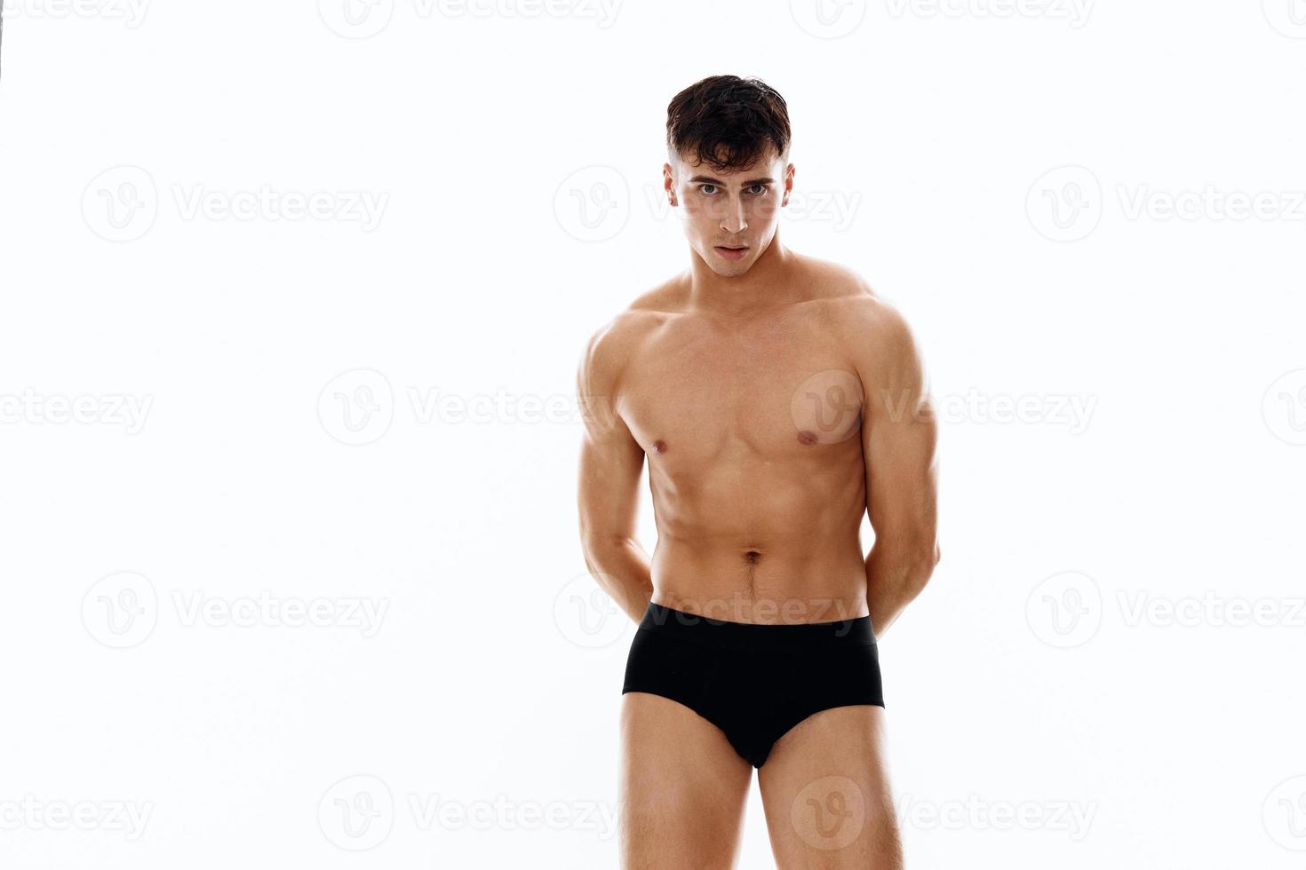 hermoso masculino atleta en negro pantalones cortos sostiene manos detrás su espalda en un blanco antecedentes foto