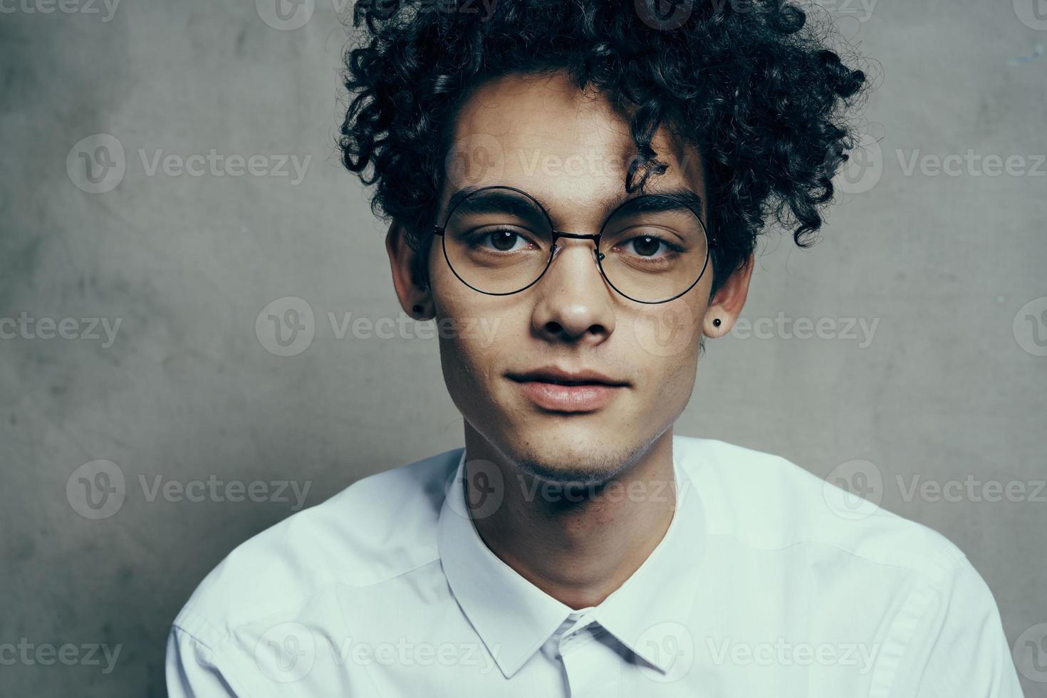 portrait of a nice guy with curly hair on a gray background and a light shirt glasses model close-up photo