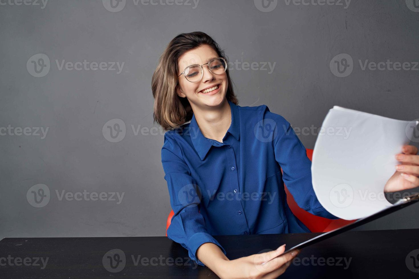 a woman in a blue shirt sits at the table a folder in her hands documents photo