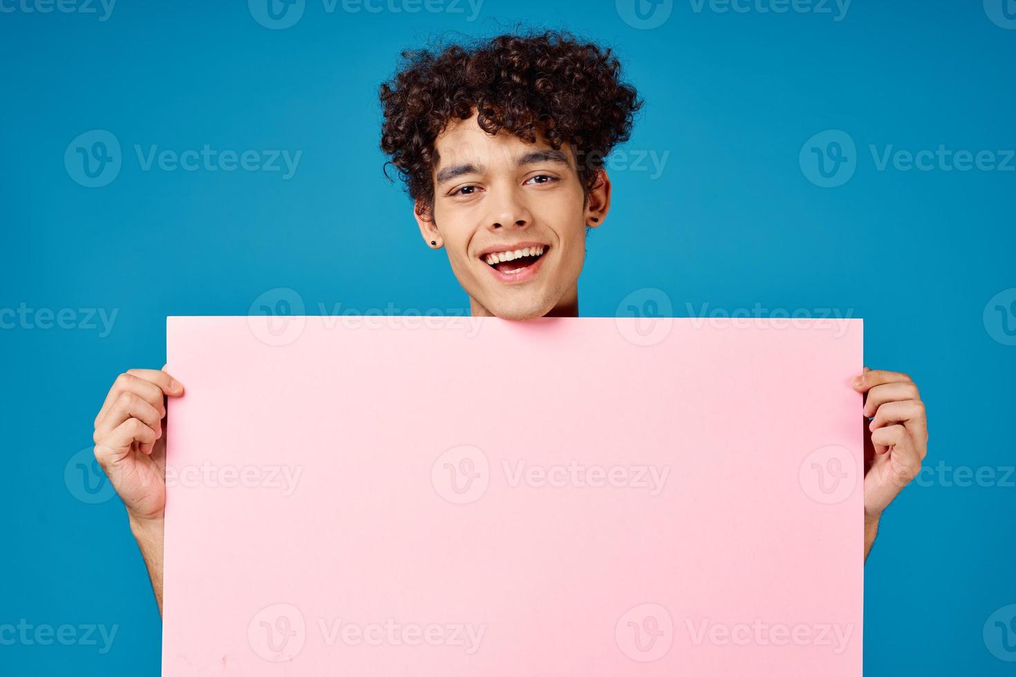 man with curly hair holding pink poster banner blue background photo