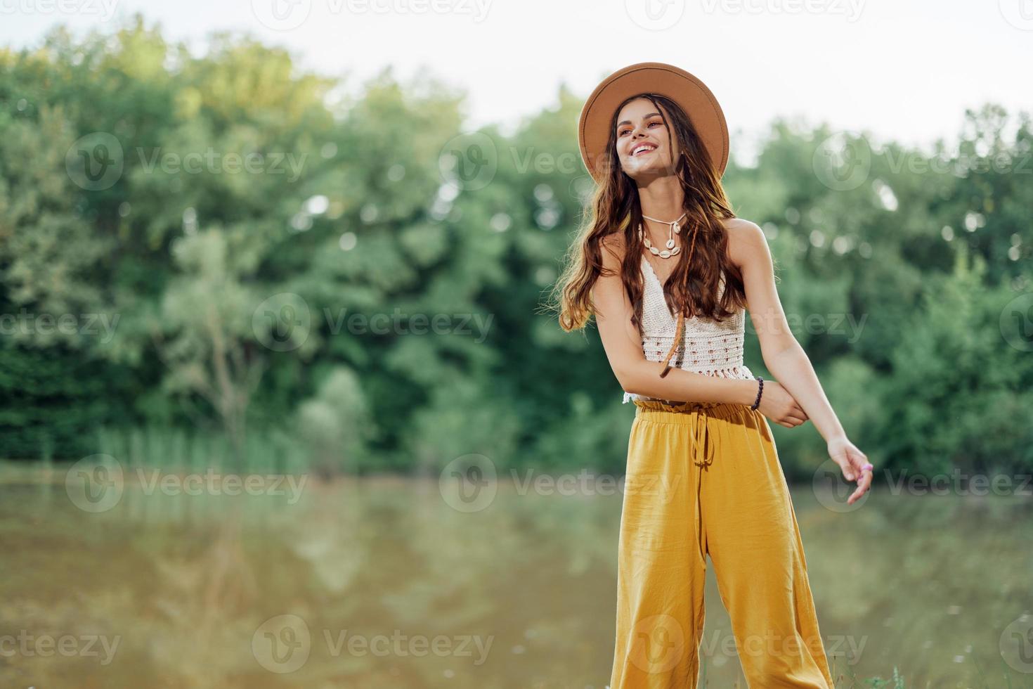 un joven mujer en un hippie Mira viajes en naturaleza por el lago vistiendo un sombrero y amarillo pantalones en el otoño foto