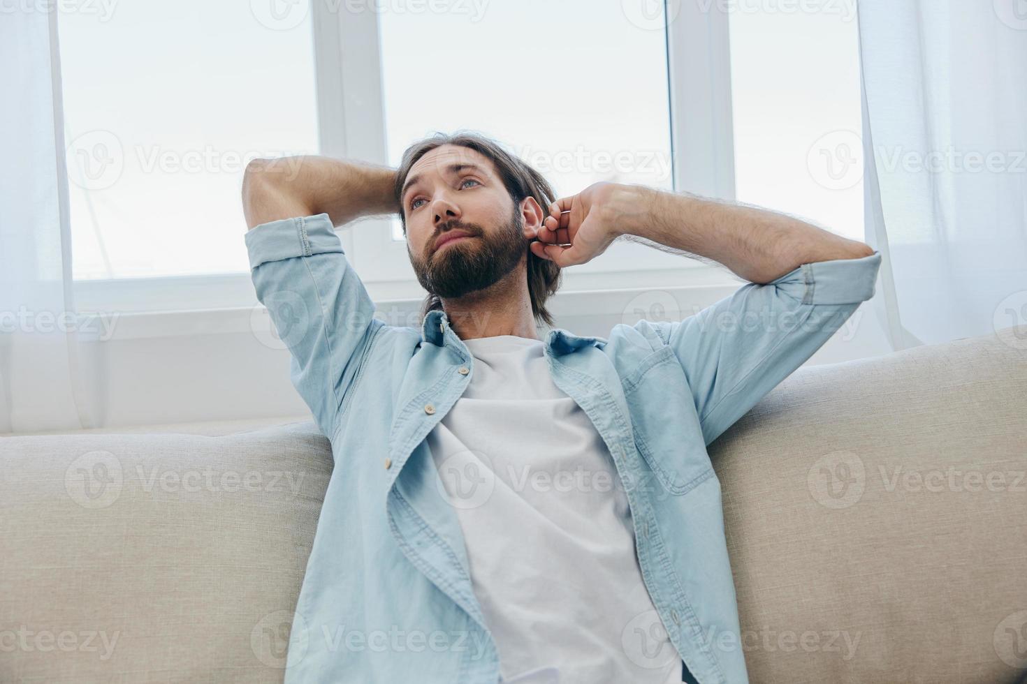A man sits on the couch yawning and stretching after a nap, lack of sleep and fatigue from work and improper daily routine. photo