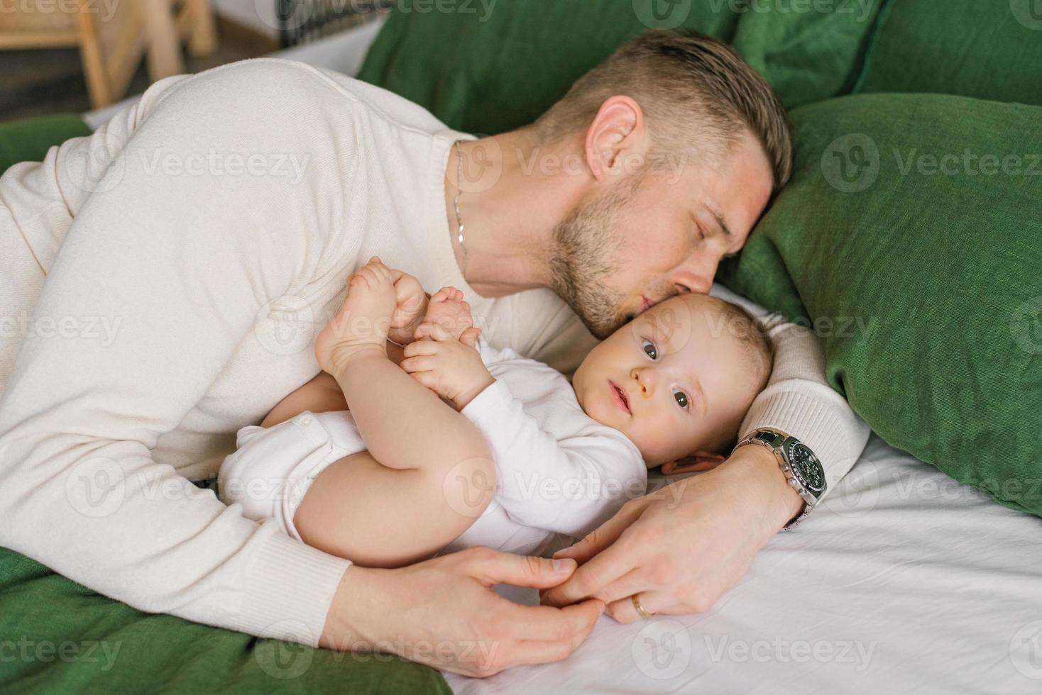 Loving father lies on the bed with his baby son, hugs him and kisses him photo