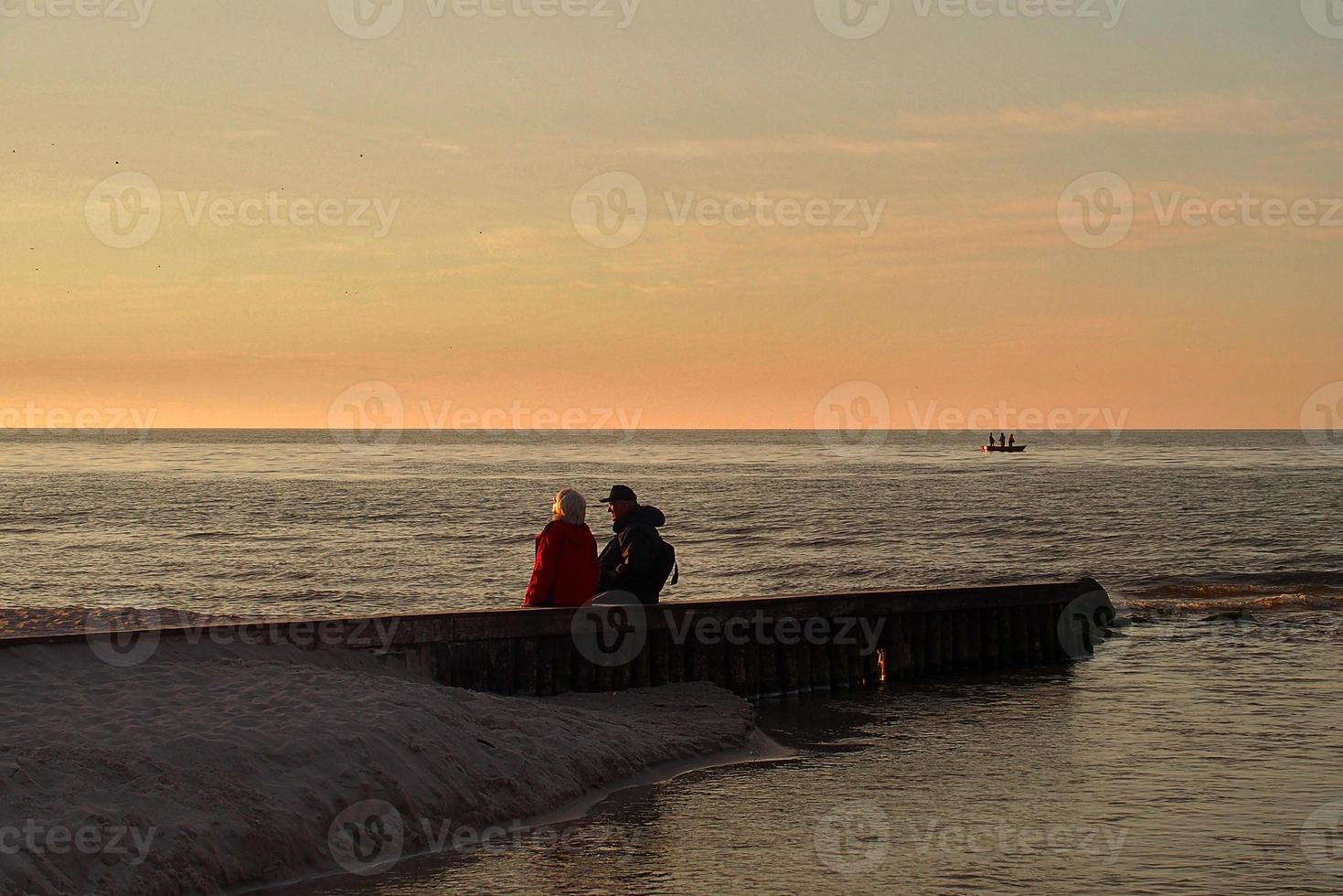 landscape with sunset on the Baltic Sea with a breakwater and a pair of people sitting on it photo