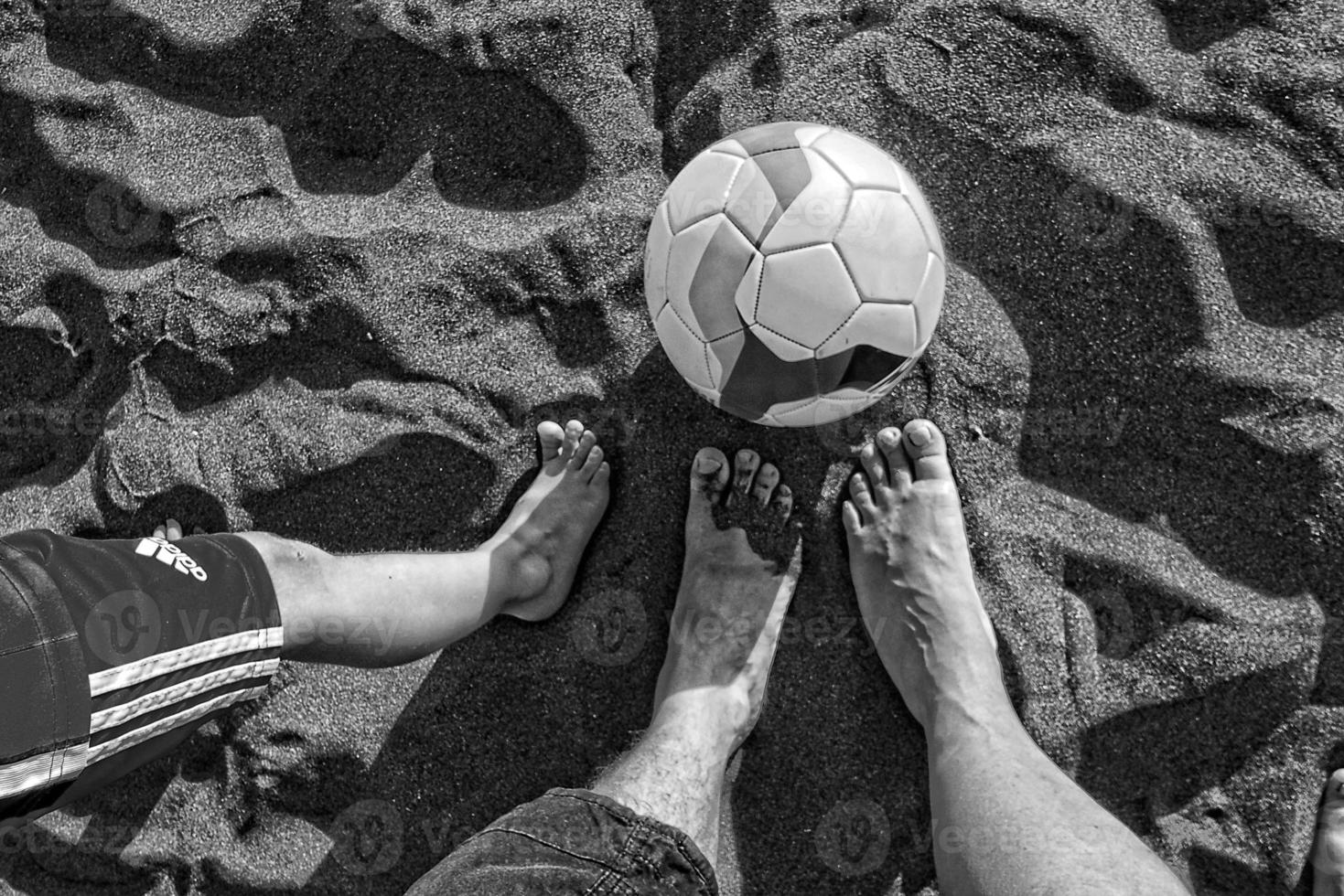 piernas mamá, padre y hijo en el playa en el arena siguiente a un fútbol pelota foto