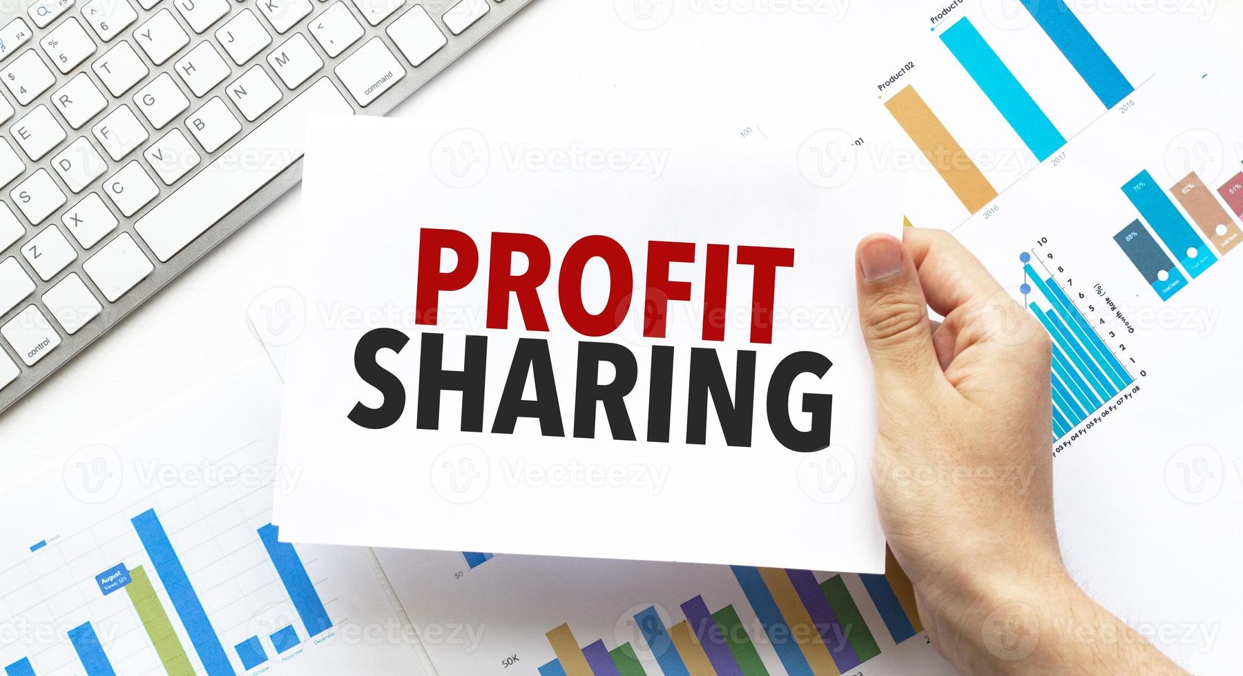 Businessman holding a card with text profit sharing .Keyboard, diagram and white background photo