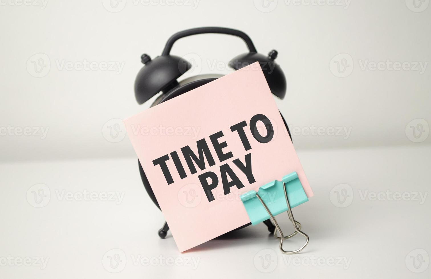 alarm clock with pink sticker with the text time to pay photo