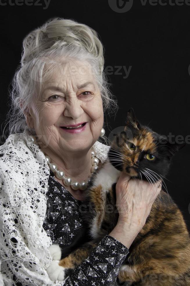 retrato de un noventa año antiguo mujer con un mascota. alegre antiguo dama con un gato. abuela en un negro antecedentes con un peludo animal. mayor belleza. el canoso bien arreglado pensionista. foto