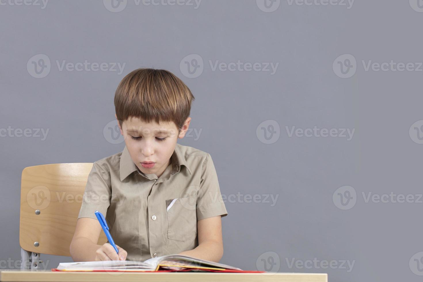 The child at the table is doing homework. Primary school student with a textbook. photo