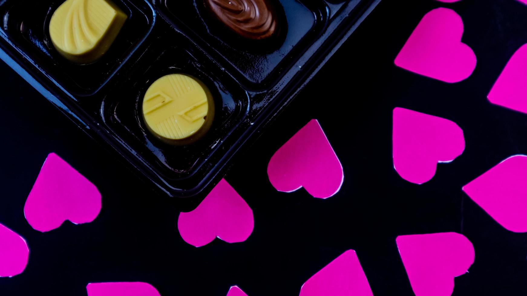 delicious chocolate surrounded by pink hearts on black background photo