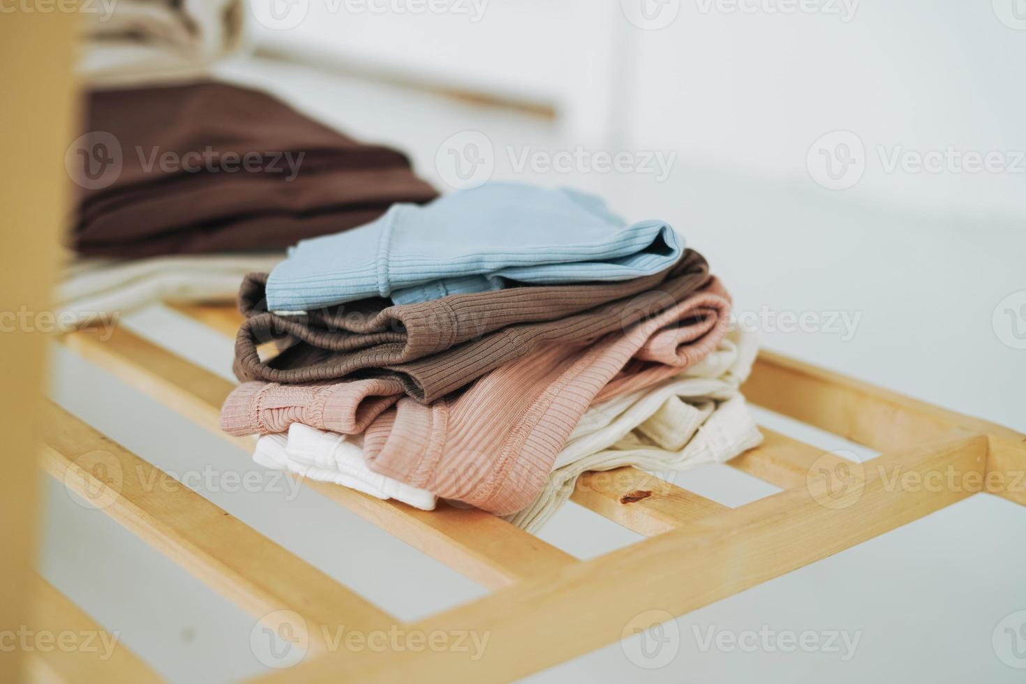 Stack of cotton tops in natural tones on wooden shelf in bright room photo