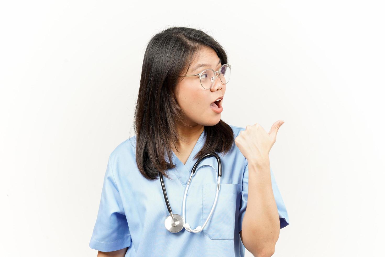 Showing and Pointing Product With Thumb Of Asian Young Doctor Isolated On White Background photo