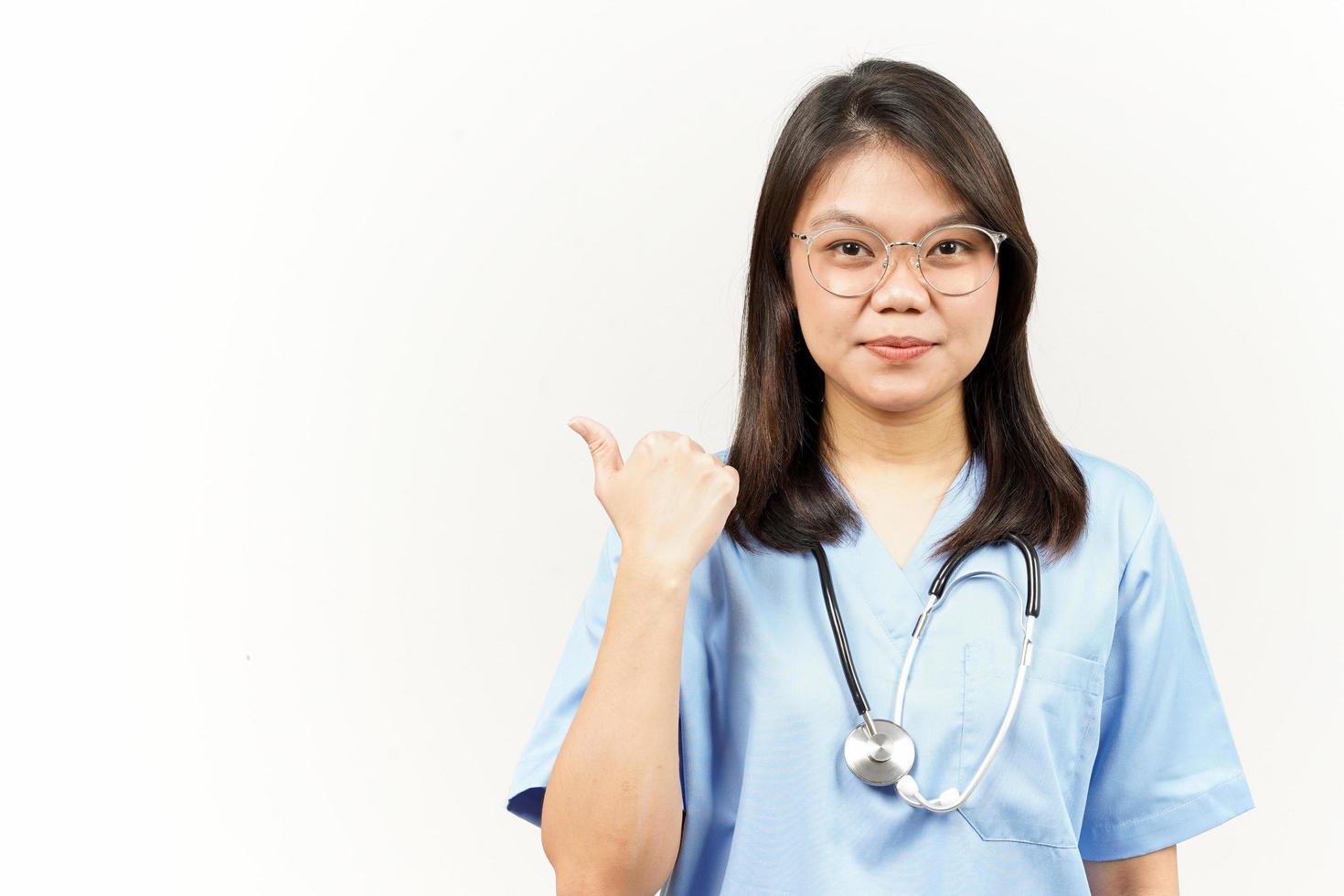 Showing and Pointing Product With Thumb Of Asian Young Doctor Isolated On White Background photo