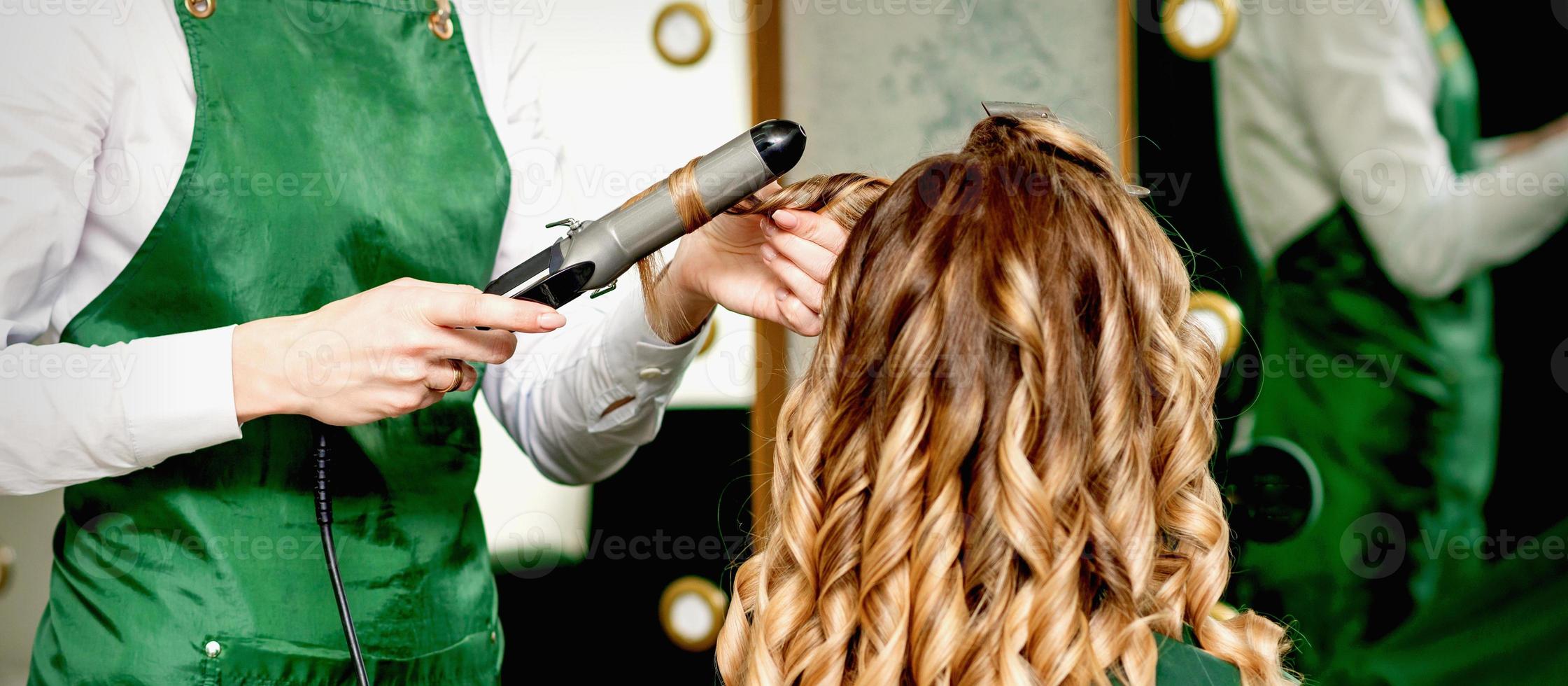 Hairdresser curling hair with curling iron photo