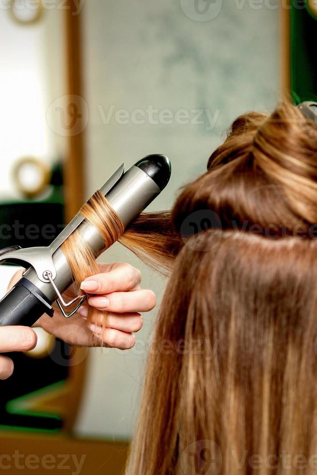 Hairdresser curling hair with curling iron photo