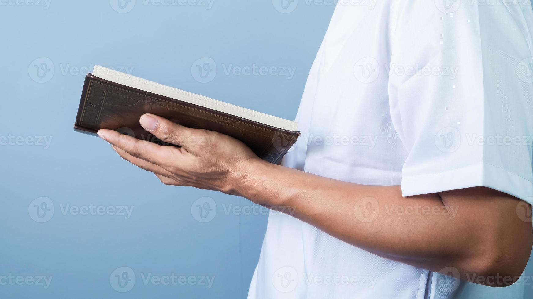 Muslim man reading holy book Koran, isolated on blue background photo