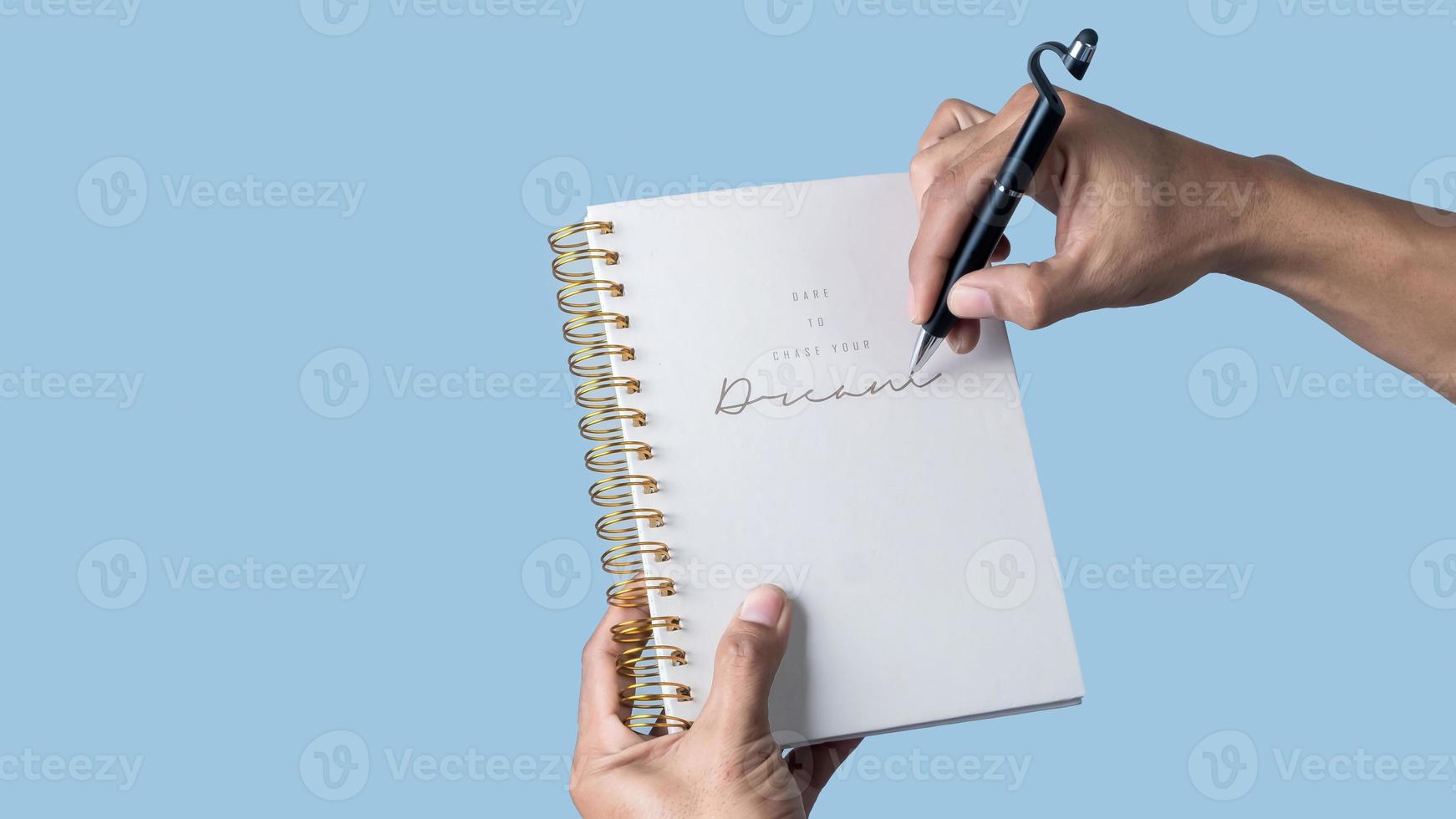 Man hand holding a pen and writing on a notebook isolated on blue background. photo