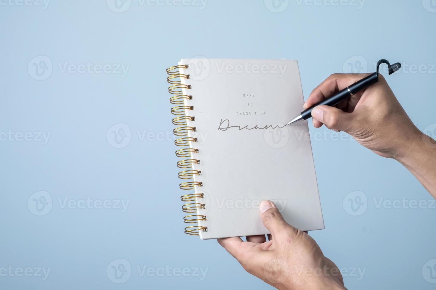 Man hand holding a pen and writing on a notebook isolated on blue background. photo