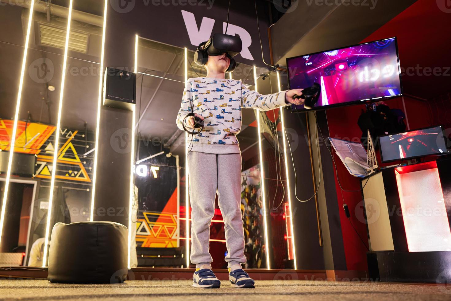 Boy kid playing game using virtual reality headset and gamepads in playing club. photo