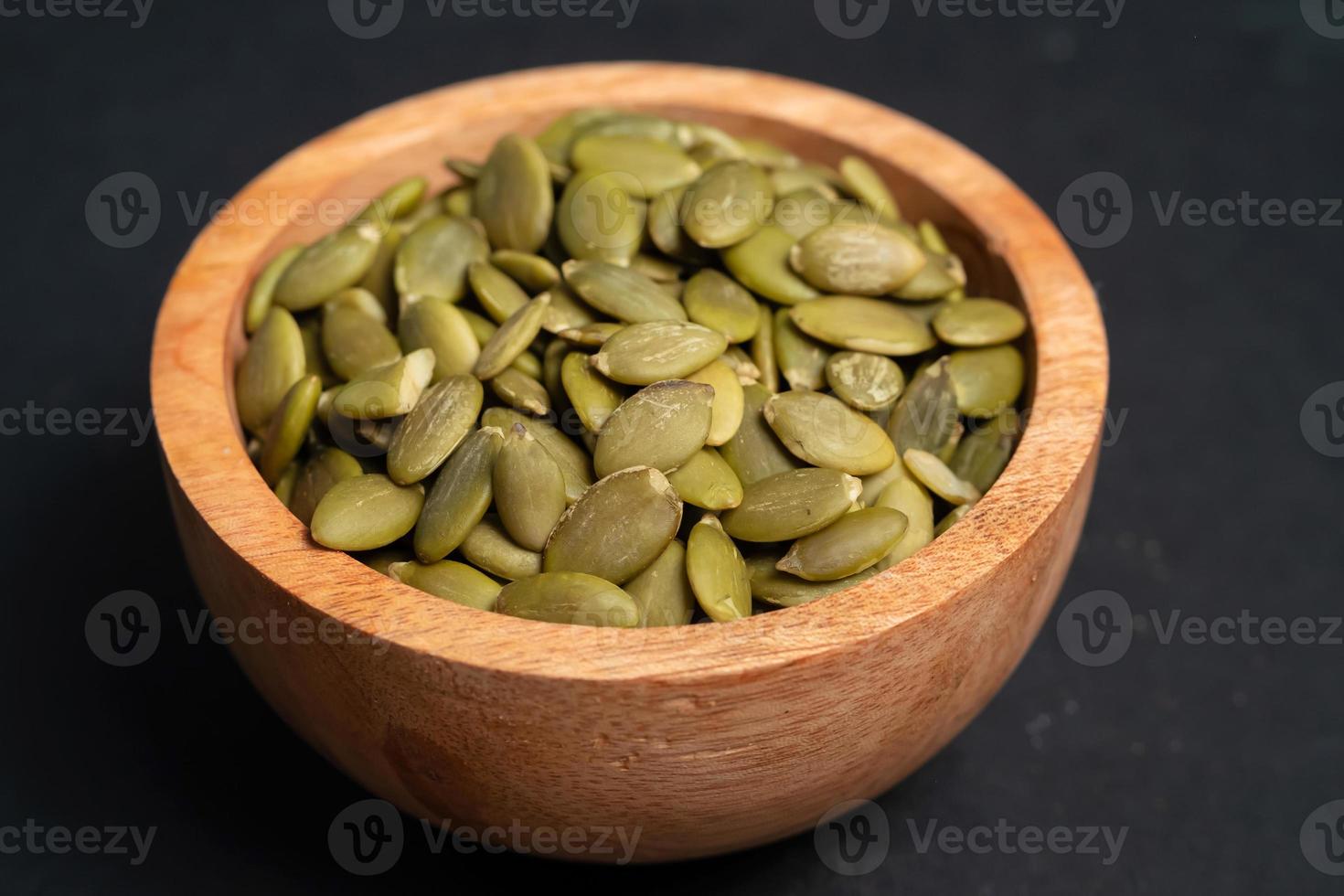 Pumpkin seeds in a wooden bowl on a dark background photo
