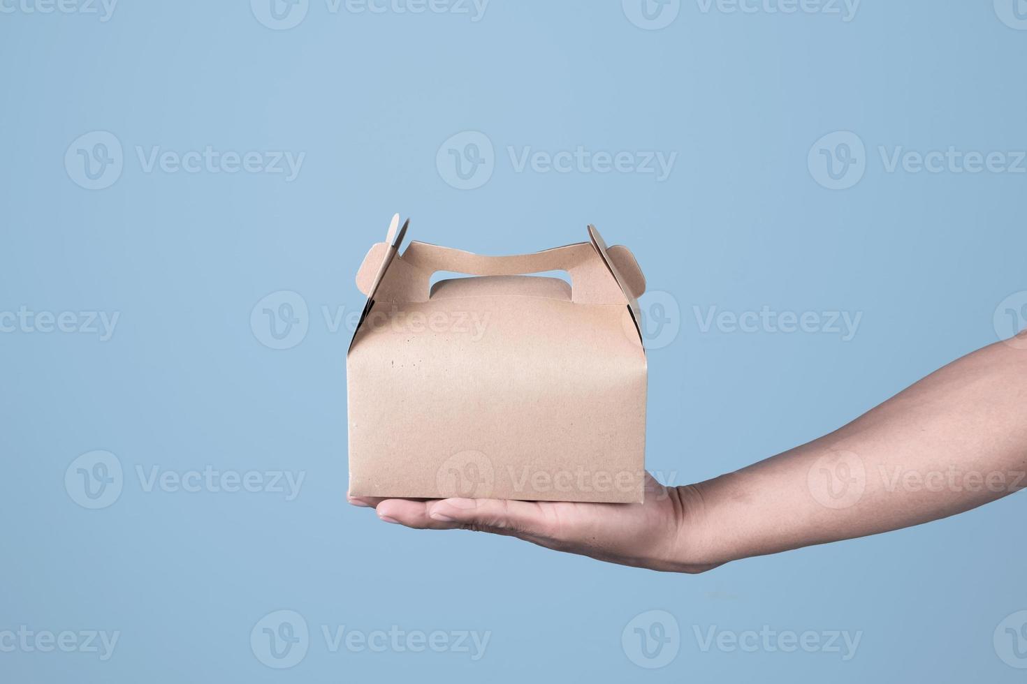 Male hand holding brown ecological package box made of natural cardboard on light blue background. Packaging, shopping, Food delivery concept photo